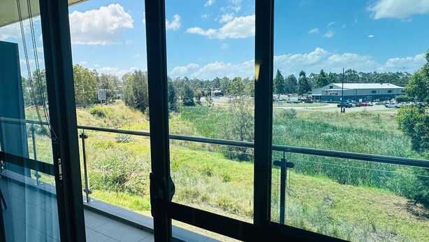 Vista da un balcone con ringhiera in metallo, su una zona verdeggiante con un edificio all'orizzonte.