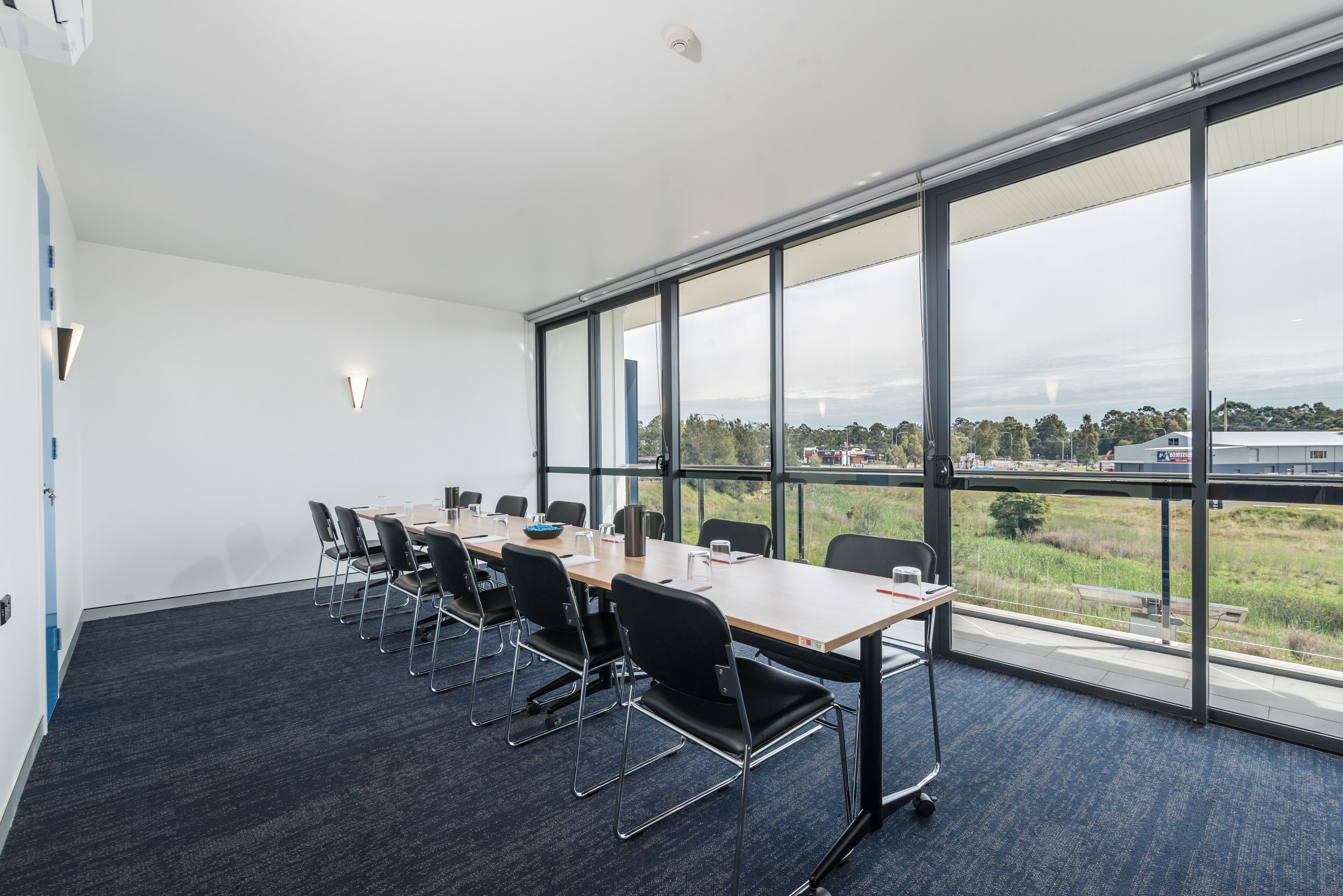 Un salón de conferencias con una larga mesa, sillas y ventanas amplias que dan a vistas del exterior.