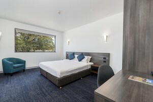 Una habitación de hotel moderna con una cama grande, un escritorio, una silla y una ventana con vistas a árboles.