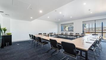 Uma sala de conferências com uma mesa comprida, cadeiras pretas e uma grande janela com vista para uma ponte.