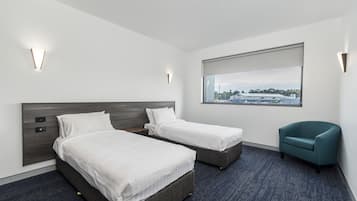 Quarto de hotel com duas camas, janela com vista e uma cadeira azul-esverdeada.
