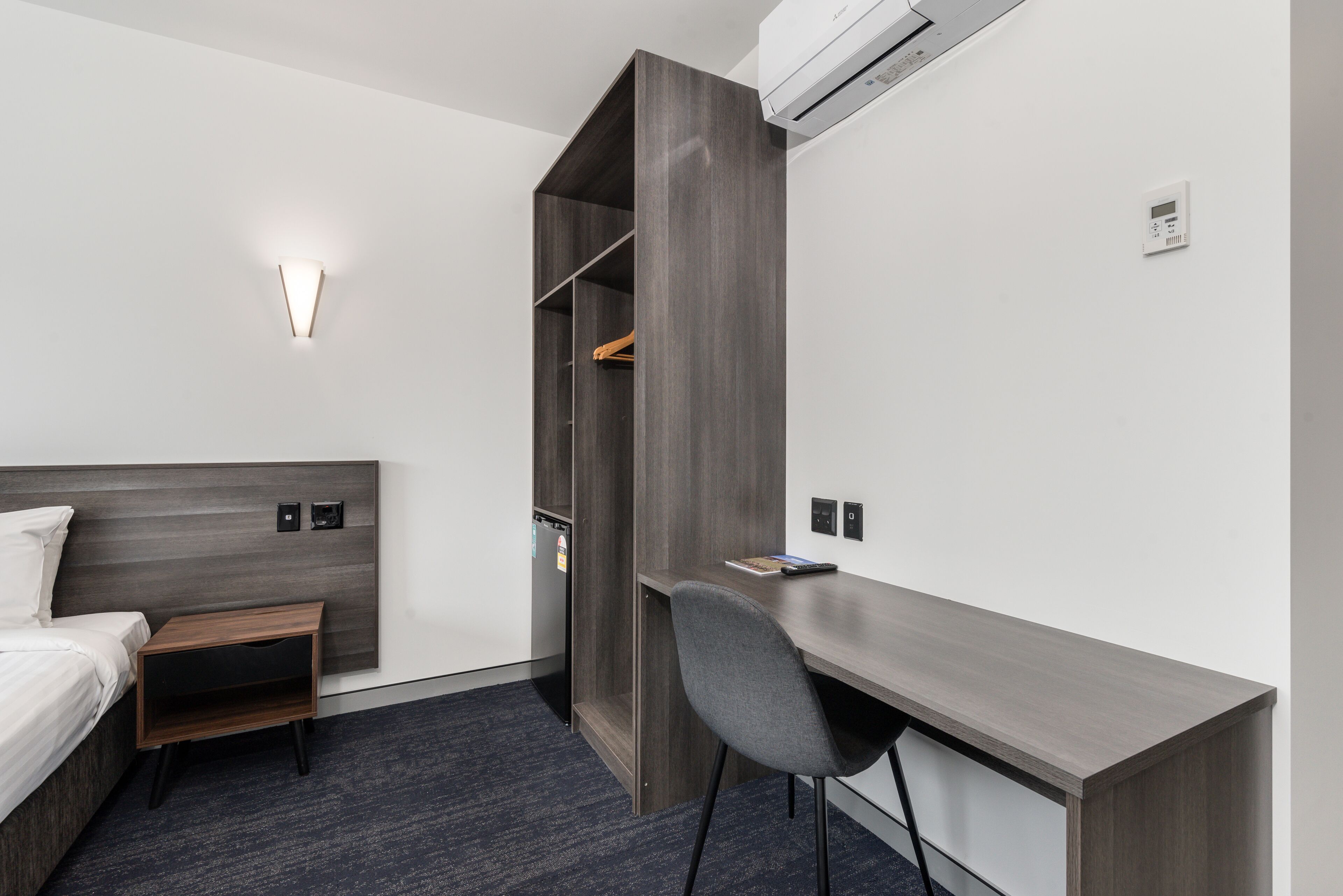 Habitación de hotel moderna con cama, escritorio, armario y aire acondicionado de pared.