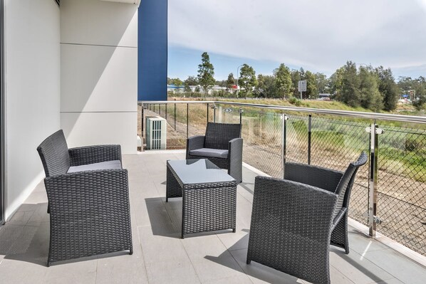 An outdoor balcony with wicker furniture and a view of a sports field.