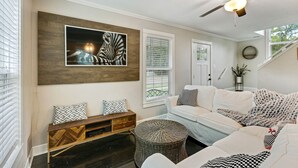 Un salon moderne avec un ventilateur de plafond, une grande œuvre d’art encadrée, un canapé blanc, un banc en bois et une petite table ronde.