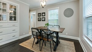 Un coin repas avec une table en bois, des chaises noires, un lustre et une plante en pot.
