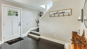 Un escalier agrémenté d’une pancarte « Bienvenue », une porte avec un paillasson et un luminaire fixé au mur.