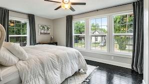 Une chambre à coucher avec un lit, un ventilateur de plafond, une fenêtre donnant sur l’extérieur et une table de chevet avec une lampe.