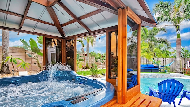 Un jacuzzi con cubierta de madera y sillas azules, rodeado de una valla de madera y palmeras.