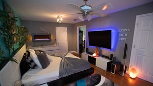 Un dormitorio moderno con cama, ventilador de techo, televisor y un cartel decorativo en la pared.
