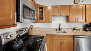 A kitchen with wooden cabinets, a microwave, a stove, a sink, and a dishwasher. - Deluxe Ocean View Condo on 31st Floor - Free Parking & Wifi! (Honolulu)