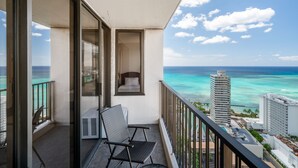 Un balcon avec une chaise et une petite table, d’où l’on peut admirer un océan turquoise et le paysage urbain.