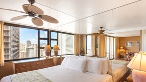 Une chambre d’hôtel dotée d’un grand lit, d’un bureau, d’une chaise, d’un ventilateur de plafond et offrant une vue sur le paysage urbain grâce à de grandes fenêtres.