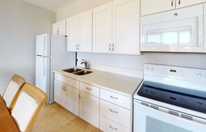 A modern kitchen with white cabinets, a stainless steel sink, a built-in oven, and a dining area with wooden chairs.