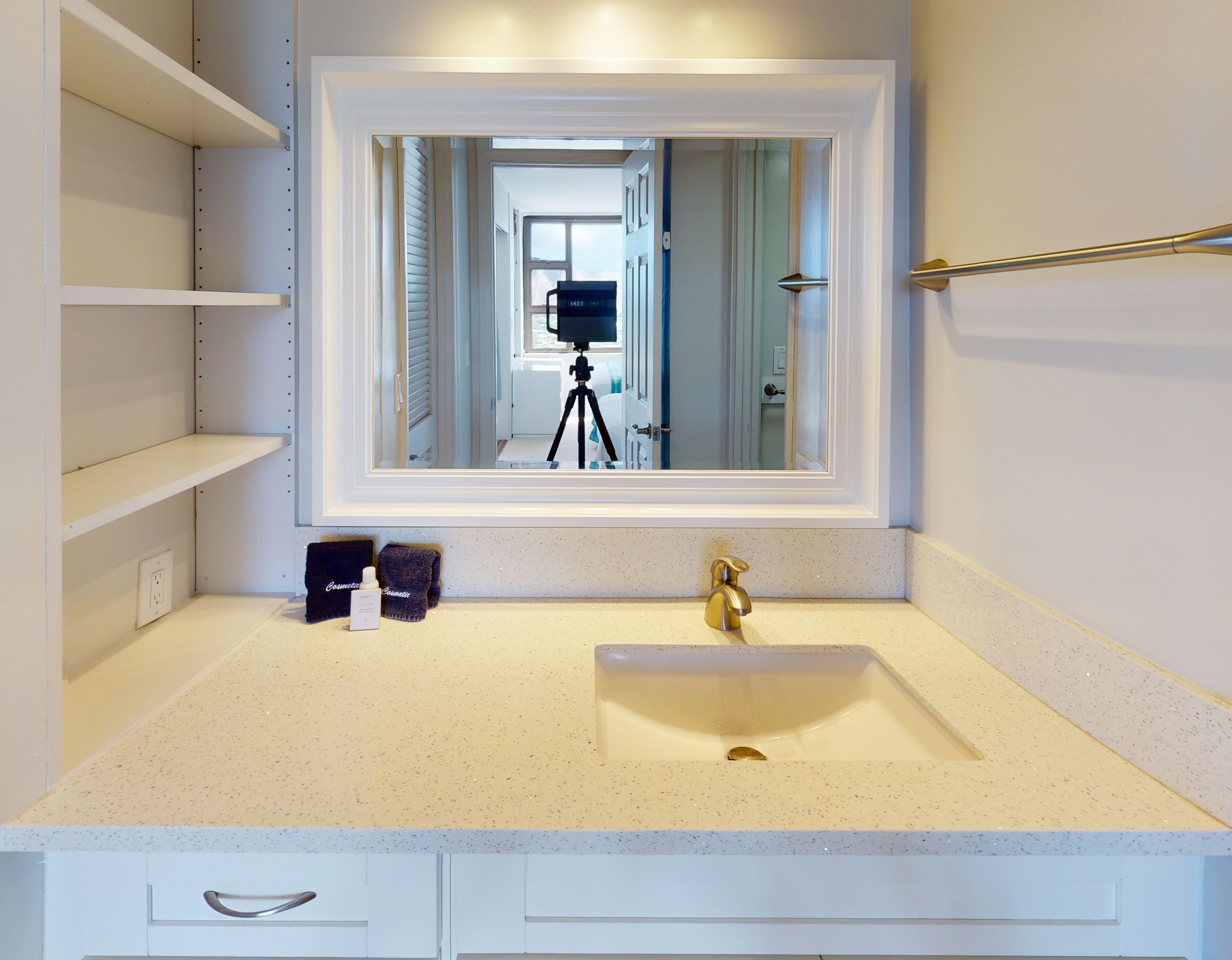 A bathroom with a white vanity, a gold faucet, and a mirror with a reflection of a room.