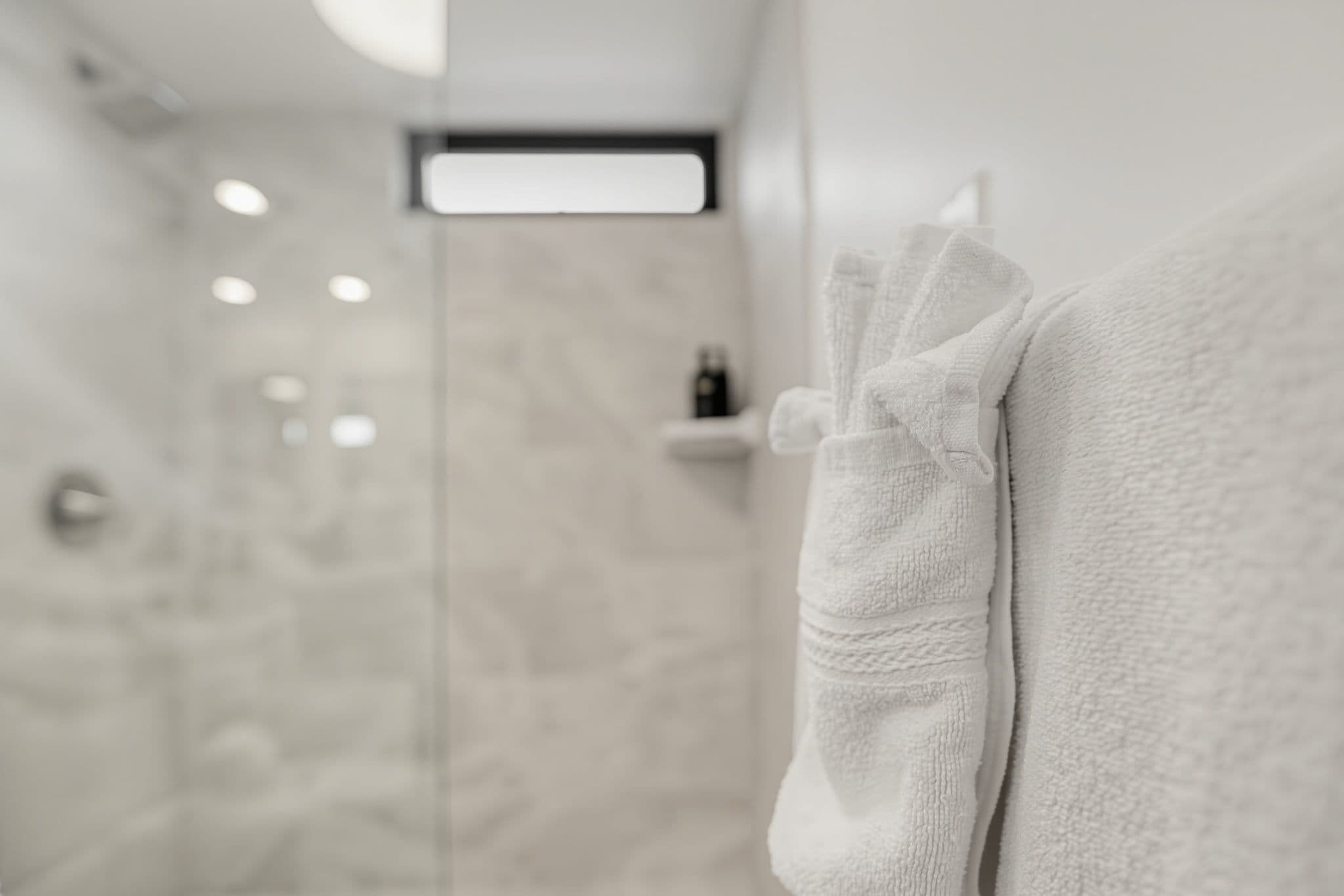 Un baño con cabina de ducha de vidrio, un perchero con una toalla doblada y un estante pequeño con artículos de tocador.