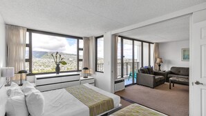 Habitación de hotel con dos camas, un balcón con vistas y una zona de estar con sofá y sillones.