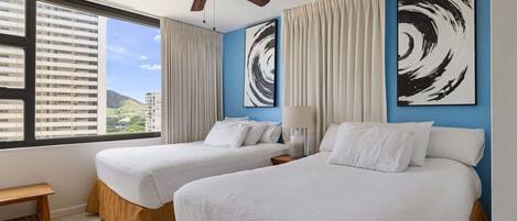 A hotel room with two beds, a ceiling fan, large windows, and abstract wall art.