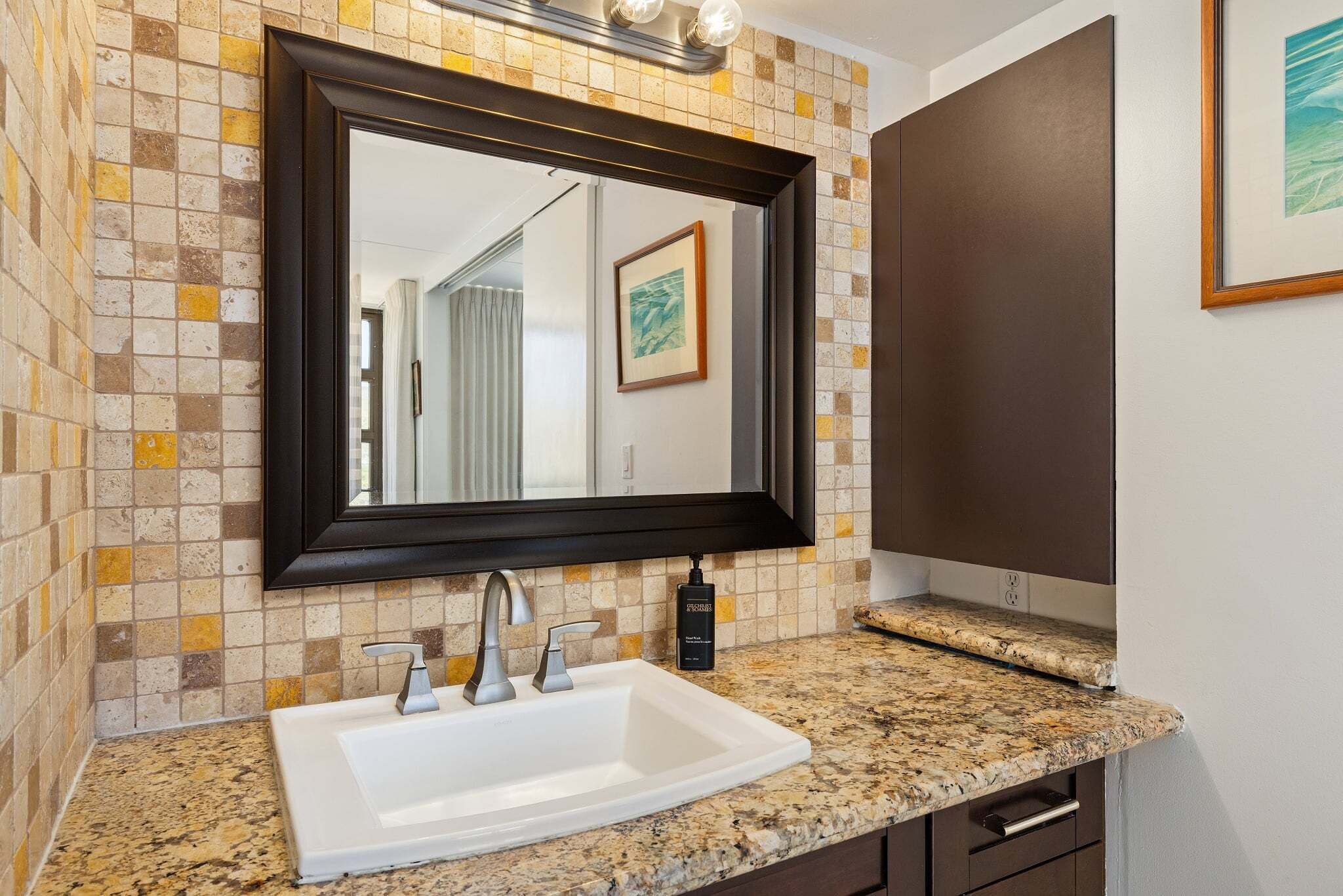 A bathroom with a white sink, a dark-framed mirror, and a tiled backsplash.