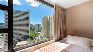 Une chambre d’hôtel dotée d’une grande fenêtre, d’un lit avec une literie blanche, et offrant une vue sur des immeubles de grande hauteur et des espaces verts.