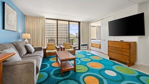 A hotel room with a sofa, chairs, a coffee table, a TV, a dresser, and a colorful carpet. - Spacious 14th Floor Corner Suite, Partial Diamond Head and Ocean Views, FREE Parking! (Honolulu)
