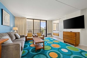 A hotel room with a sofa, chairs, a coffee table, a TV, a dresser, and a colorful carpet. - Spacious 14th Floor Corner Suite, Partial Diamond Head and Ocean Views, FREE Parking! (Honolulu)