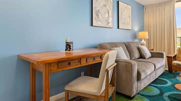 Une pièce avec un bureau en bois, un canapé gris et deux tableaux abstraits accrochés au mur.
