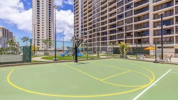 Un terrain de basket en plein air avec un toboggan bleu, entouré d’un immeuble de grande hauteur.