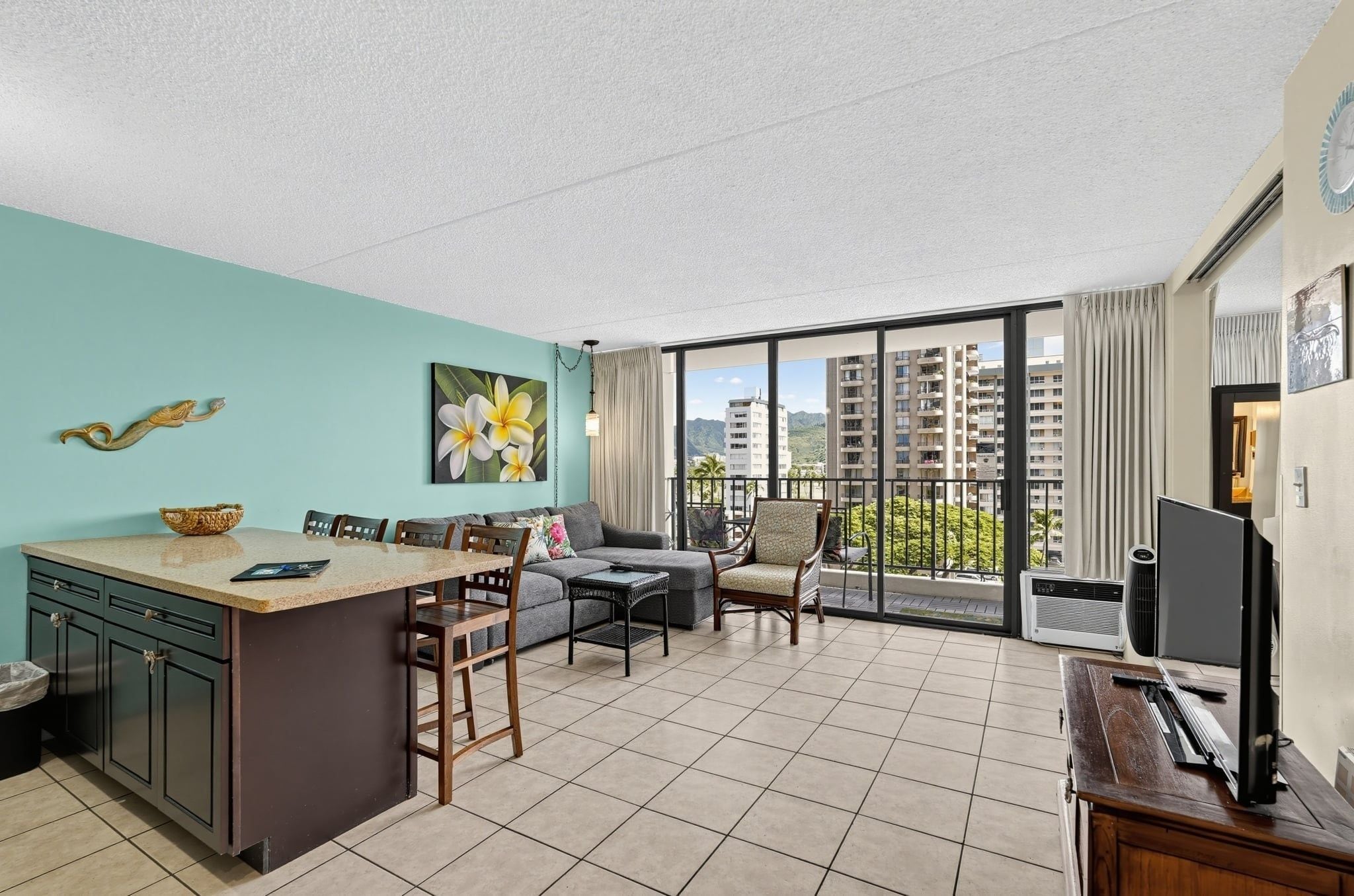 A modern hotel room with a kitchen area, a dining space, and a balcony with a city view.