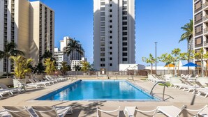 A swimming pool surrounded by lounge chairs, palm trees, and tall buildings. - Updated Waikiki Condo with Mountain Views - 22nd floor, Free parking & WiFi (Honolulu)
