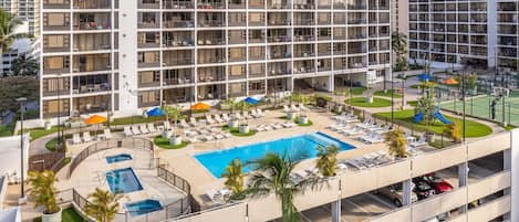 A high-rise hotel with a rooftop pool, sun loungers, and a landscaped area.