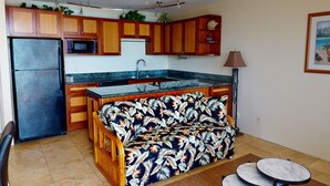 A compact kitchen with wooden cabinets, a black refrigerator, a microwave, and a built-in bench with a leaf pattern.