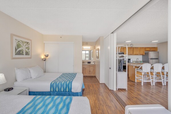Een hotelkamer met twee bedden, een kitchenette en een eethoek met stoelen.