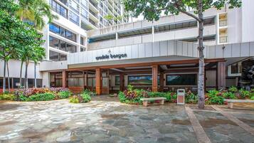 A modern building with a covered entrance, stone-paved courtyard, and lush greenery.
