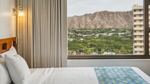 A hotel room with a bed, a window with a view of a mountainous landscape and a city below. - Gorgeous High Rise Waikiki Condo with Ocean and Diamond Head Views (Honolulu)
