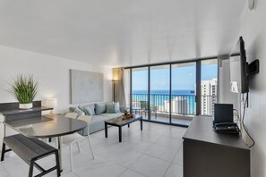 Enjoy ocean views from the large window in this stylish living area, featuring a sofa, flat-screen TV, and a glass-top coffee table.