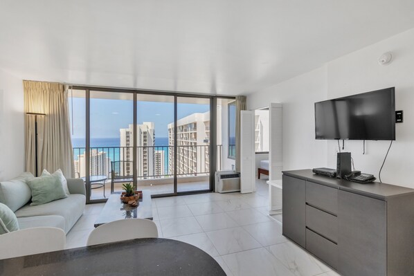Enjoy a panoramic view of the city and sea from this stylish living room with a large window, flat-screen TV, and comfortable seating area.