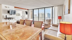 Une chambre d’hôtel moderne dotée d’une grande table à manger, de sièges confortables, d’un téléviseur fixé au mur et d’un balcon offrant une vue sur la ville.