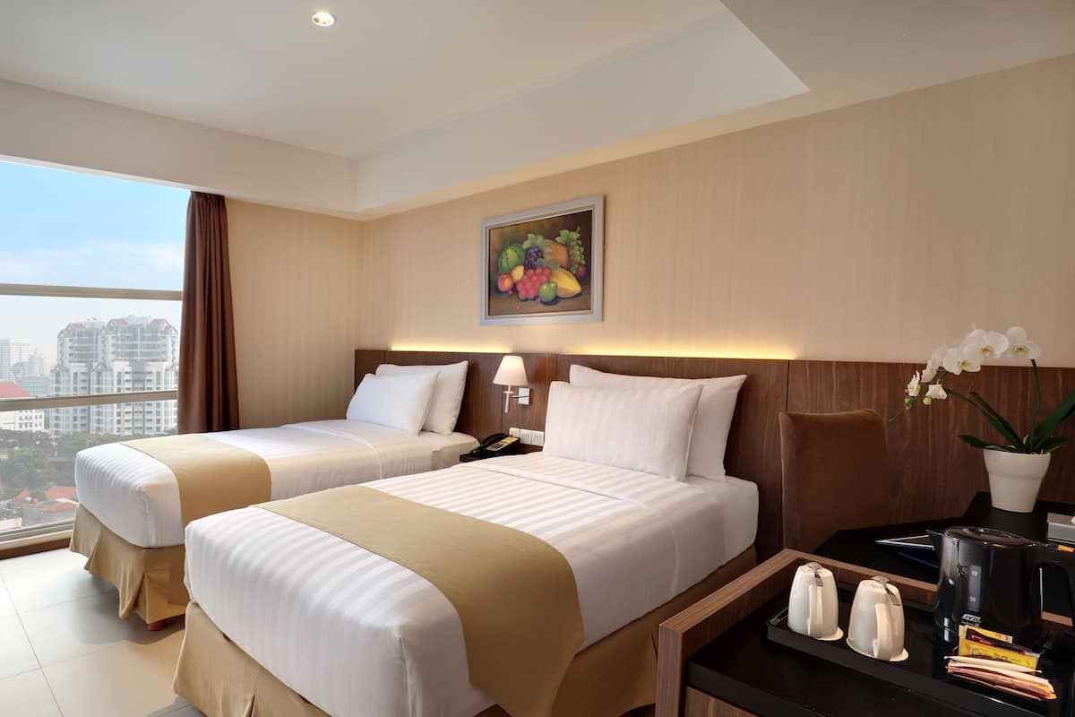 A hotel room with two beds, a desk with a coffee maker, a phone, and a painting on the wall.