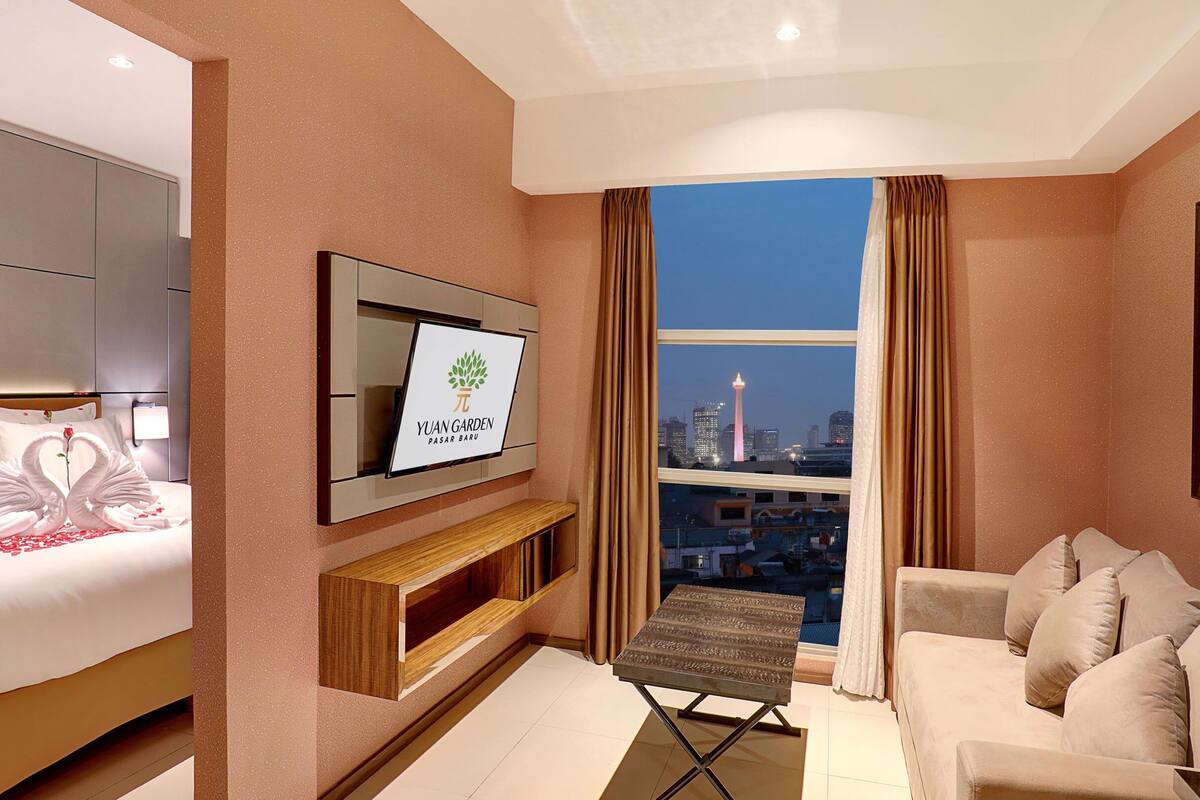 A hotel room with a bed, a sofa, a TV, a small table, and a city view.