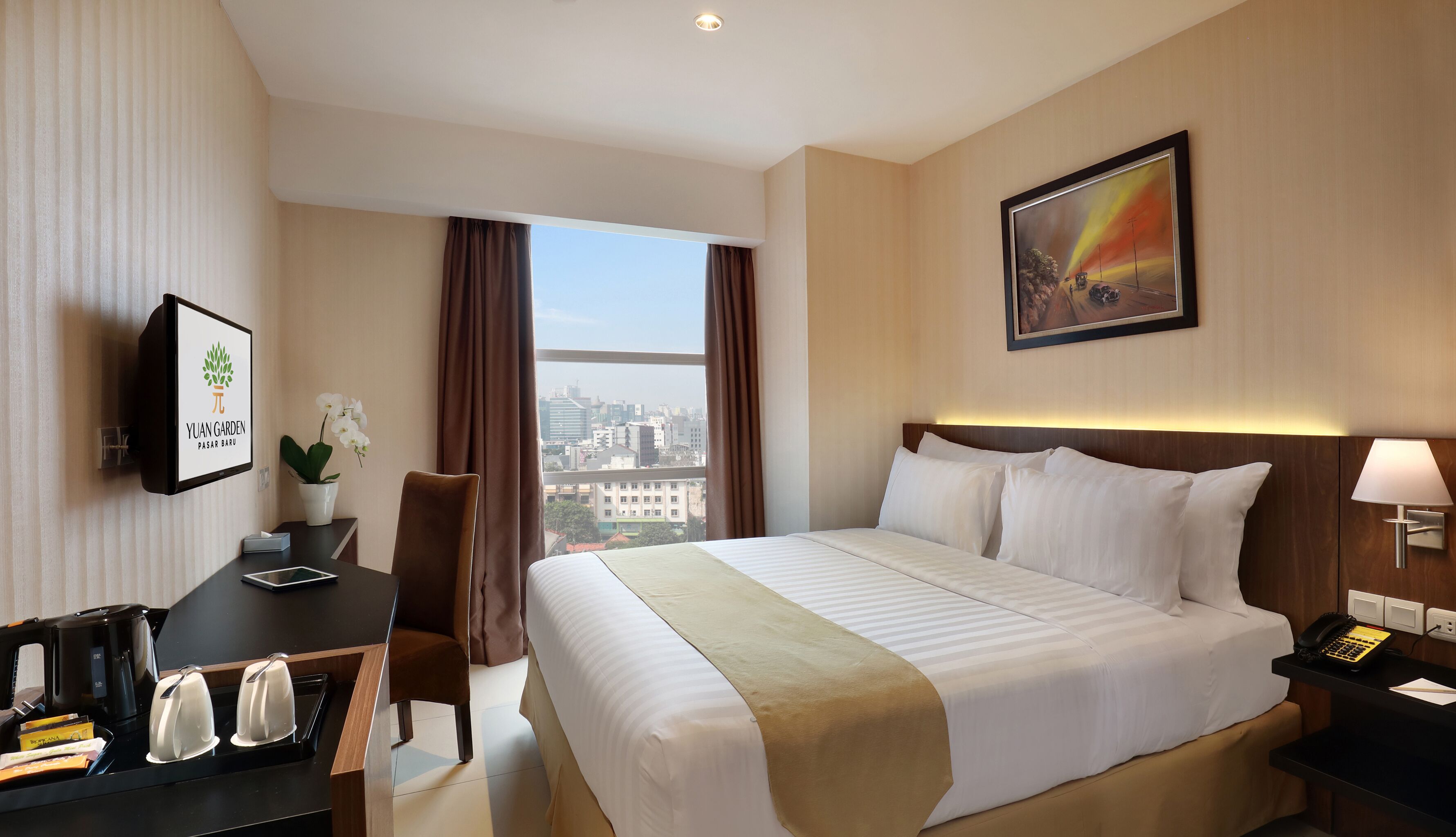 A hotel room with a bed, a desk with a telephone, a chair, a window with curtains, and a painting on the wall.