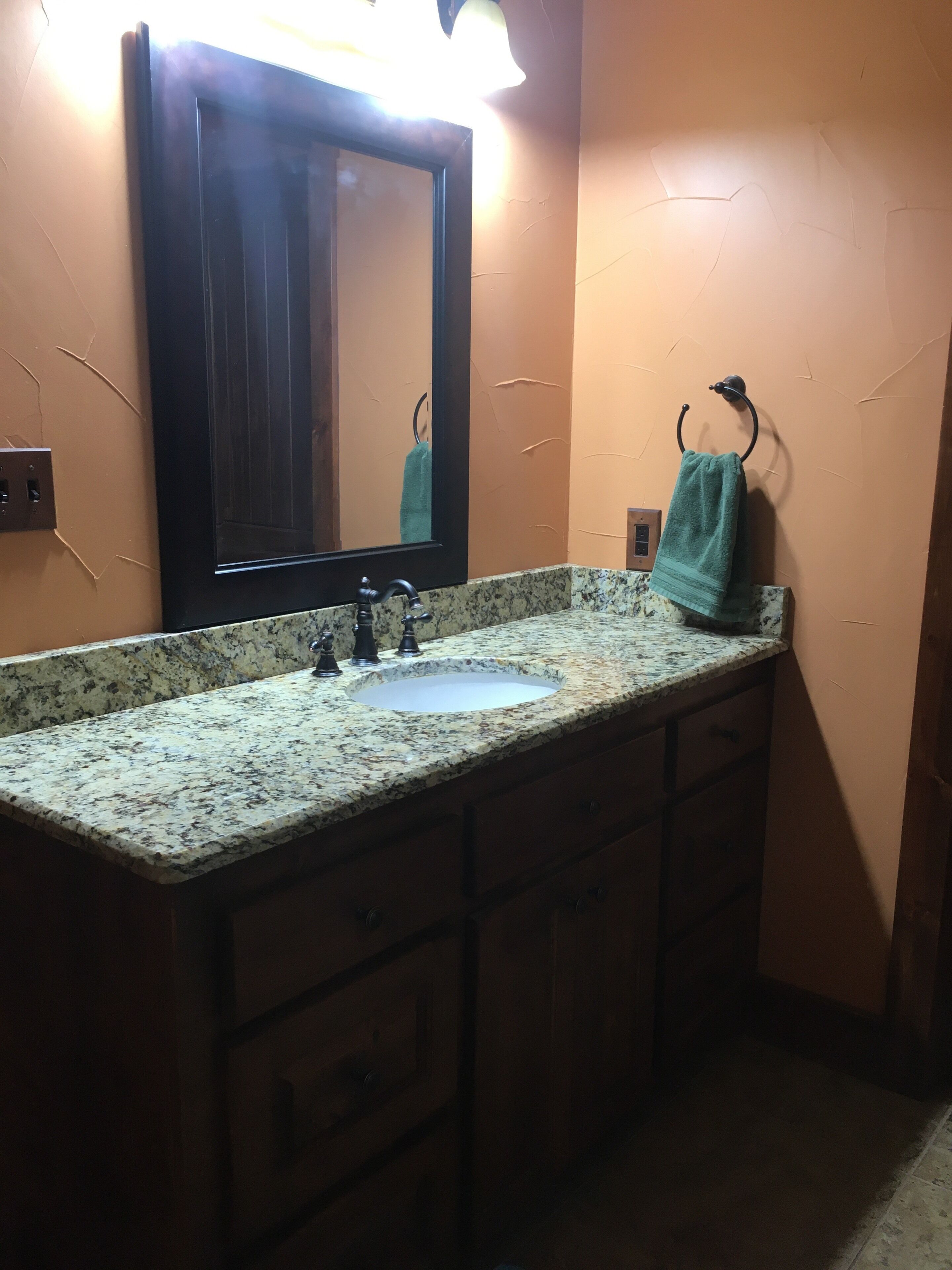 A bathroom with a granite countertop sink, a large mirror, and a towel hanging on a rack.