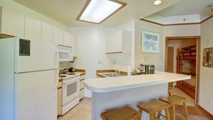A kitchen with white cabinets, a central island with stools, a microwave, and a stove.