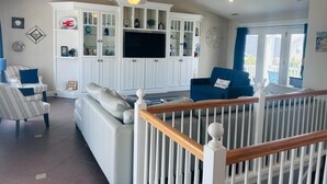 A living room with a white entertainment center, a sofa, a blue armchair, and a white railing.