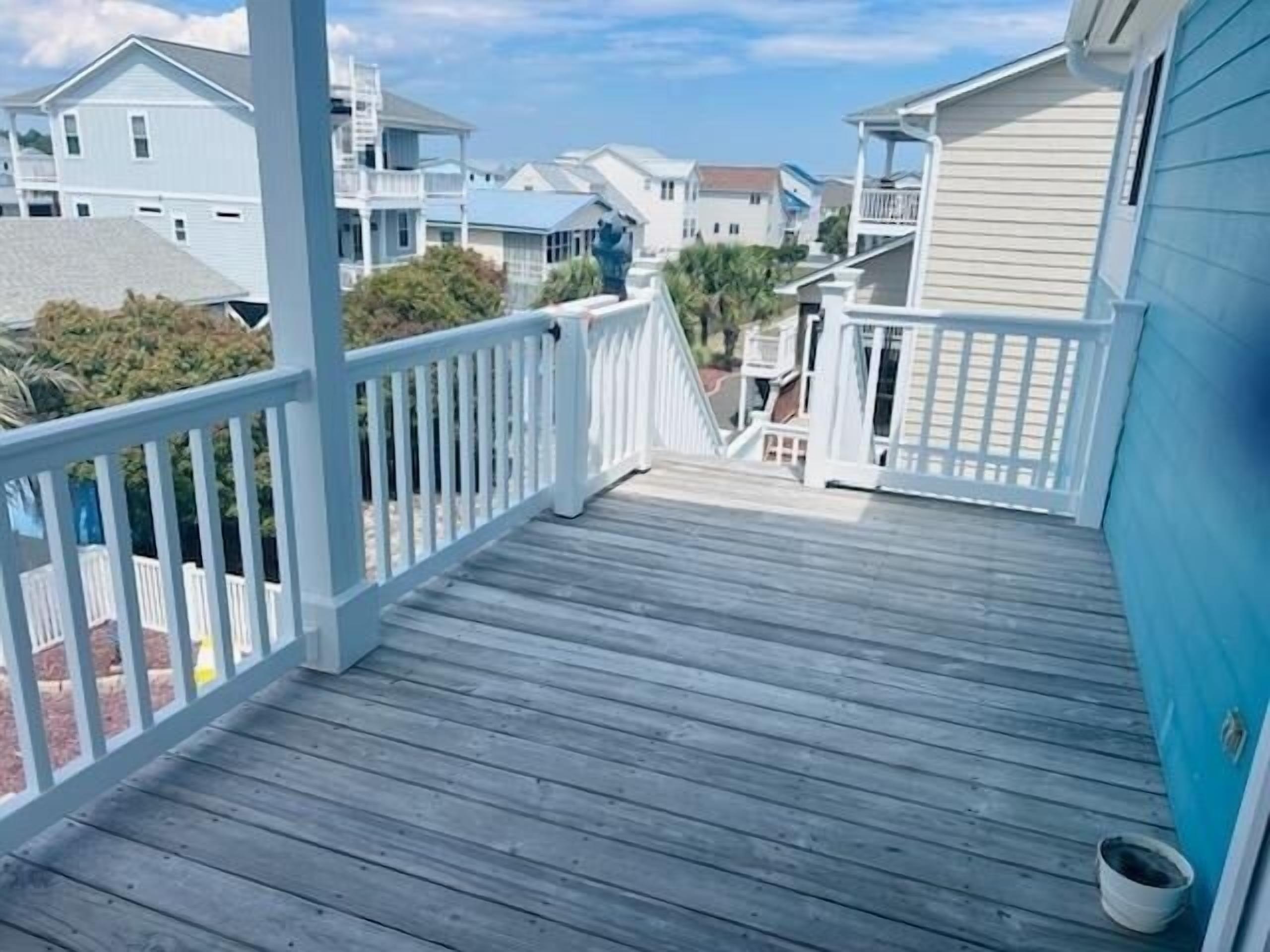 A wooden deck with white railings leading to a building with a blue exterior.