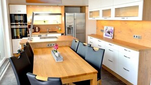 Eine moderne Küche mit einem Holztisch, schwarzen Stühlen, weißen Schränken, Edelstahlgeräten und einem gerahmten Bild auf der Arbeitsfläche.