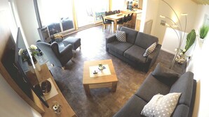 Ein geräumiger Wohnbereich mit einer Sofagarnitur, einem Couchtisch und einem Fernseher. Im Hintergrund ist eine Essecke mit Tisch und Stühlen zu sehen.