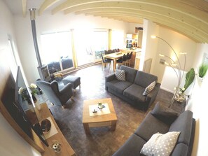 Un vaste espace de vie comprenant un canapé, une table basse et un téléviseur. On aperçoit également un coin repas avec une table et des chaises à l’arrière-plan.