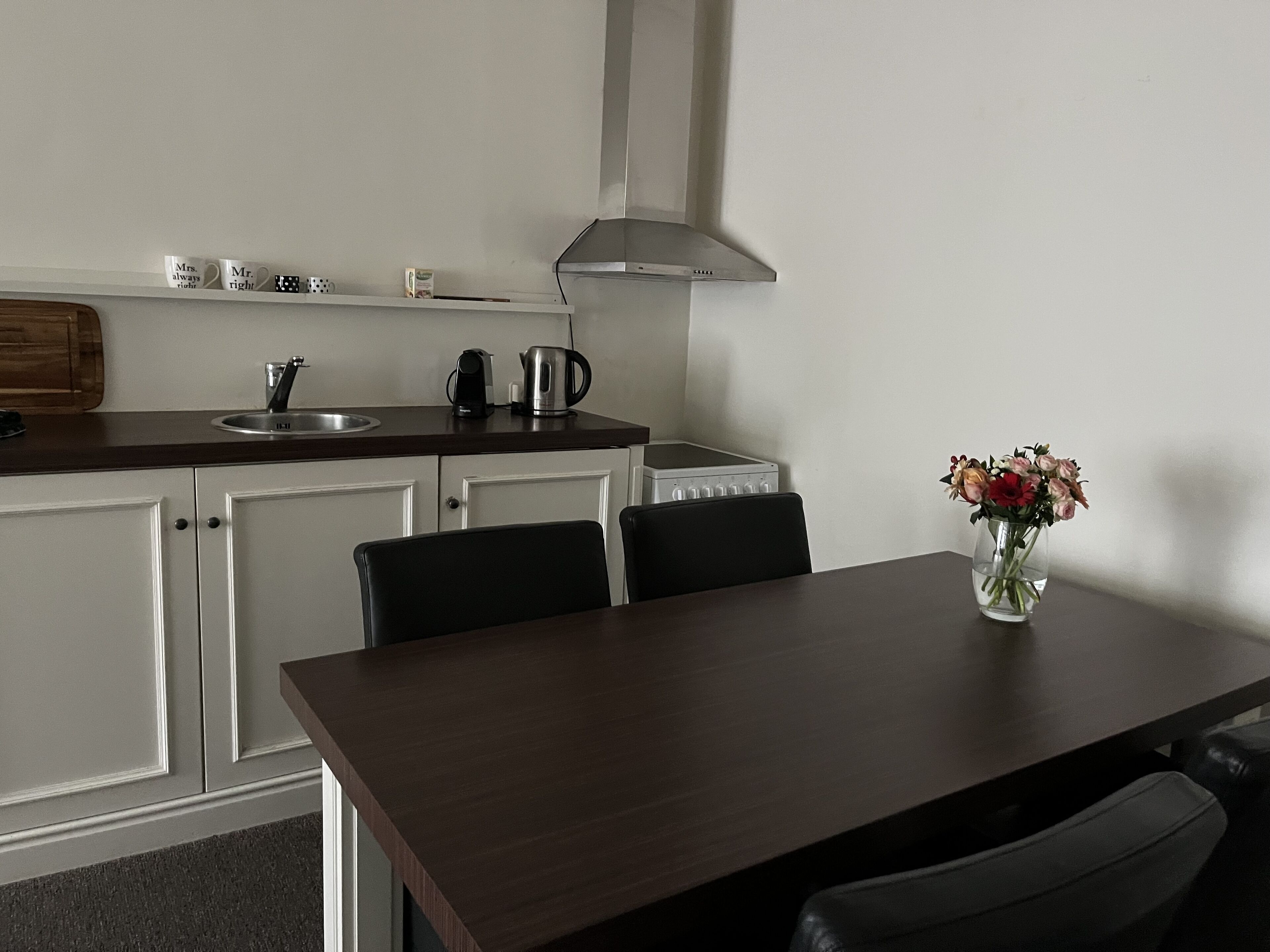 Een moderne keuken met witte kastjes, een donker houten tafel en een bloevas.