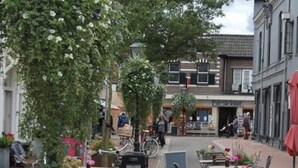Un área de café al aire libre con mesas y sillas, rodeada de edificios y árboles.