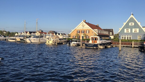 Un puerto con barcos amarrados, un muelle de madera y casas de arquitectura tradicional.